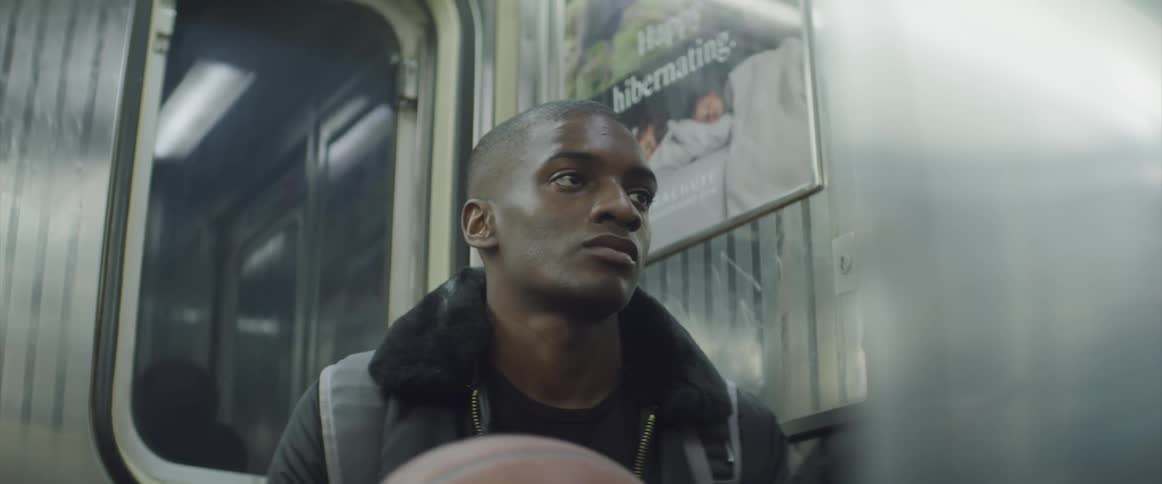 A teenager holding a basketball sits on a train