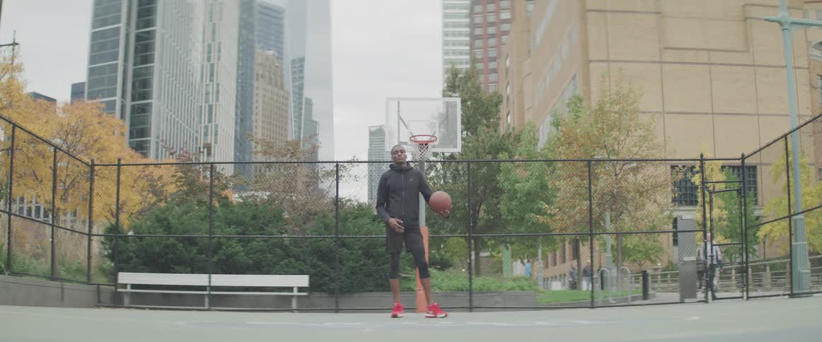 A man posing with a basketball on a public outdoor basketball court in a city