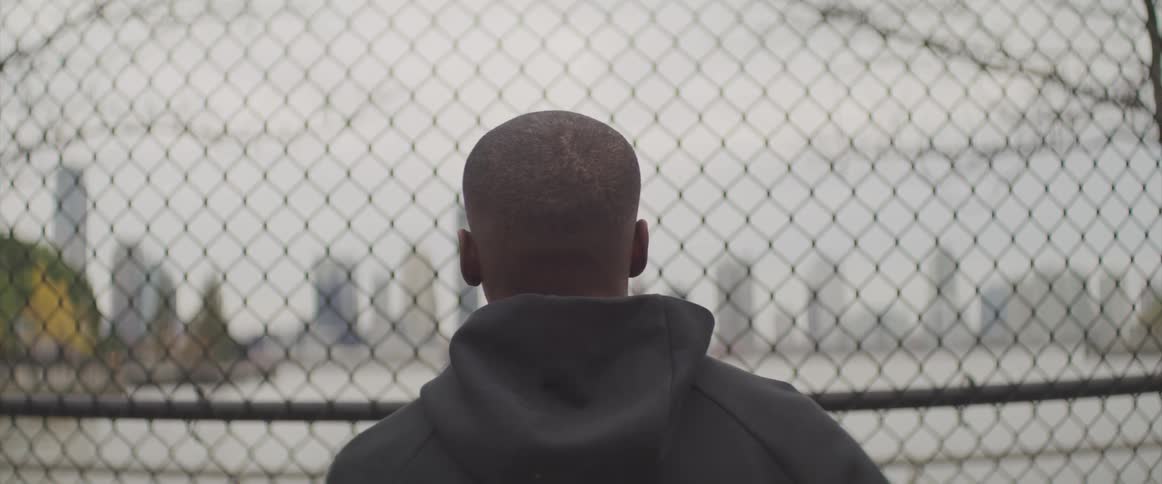 Black basketball player looks at the distant high rise buildings in the public basketball court