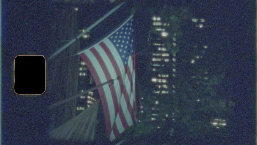 Two flags hang from the side of a building in a downtown area