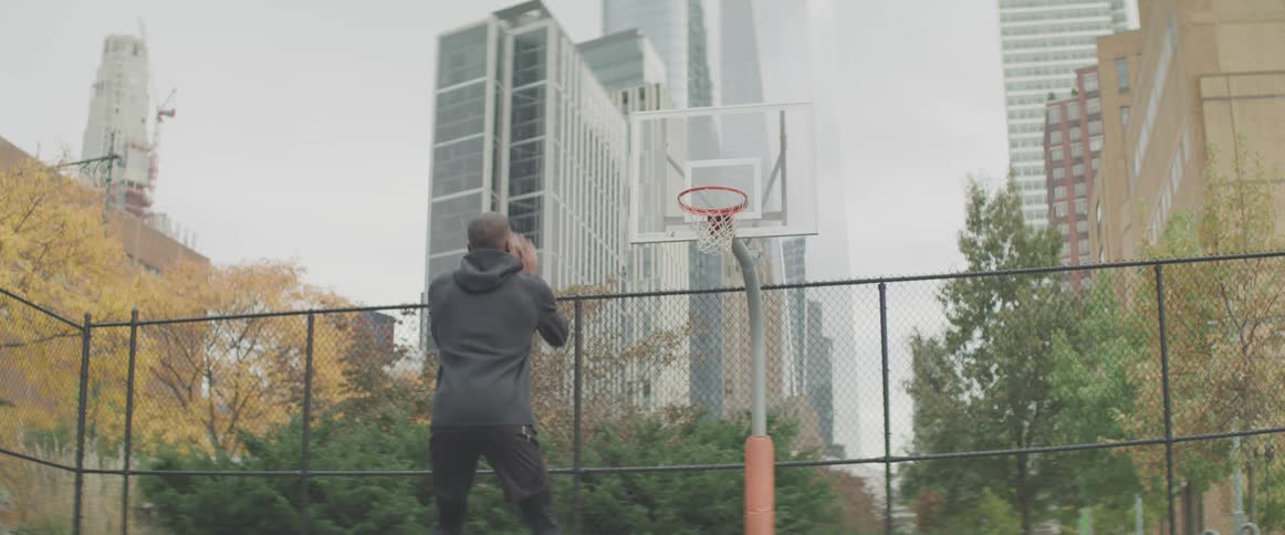 A man shoots a basketball at a hoop in a public city park