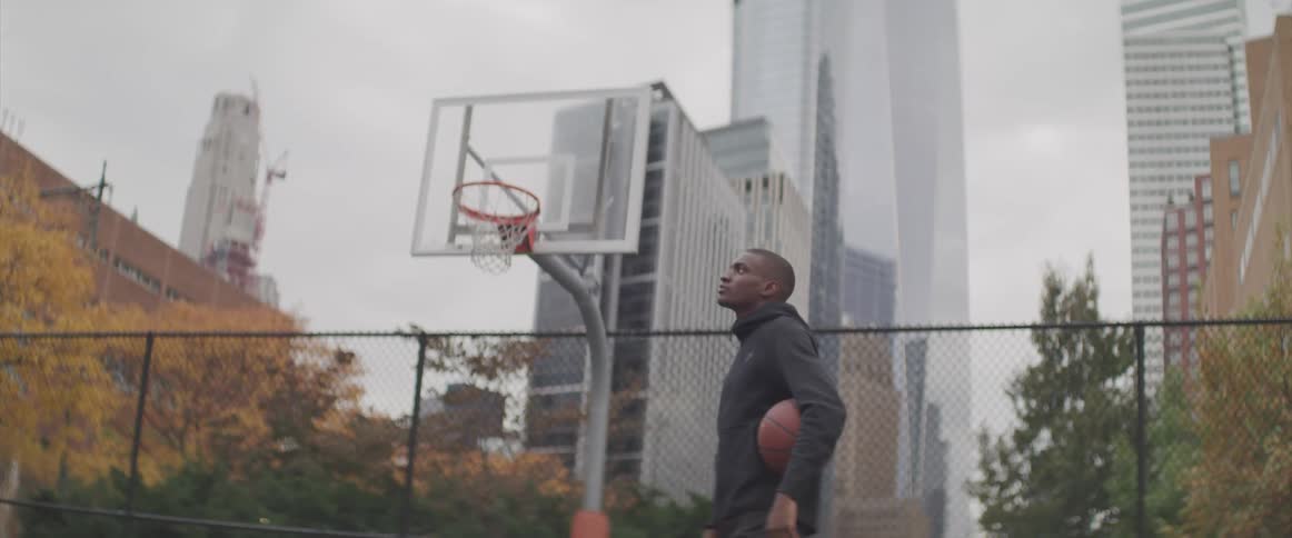 A man stands by a basketball hoop holding a ball and looking up to the sky