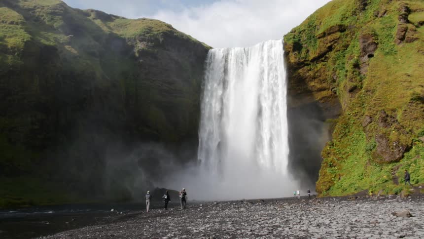 People are standing at the foot of a large waterfall