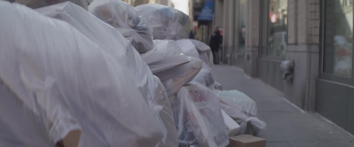 A city pavement with white trash bags piled up