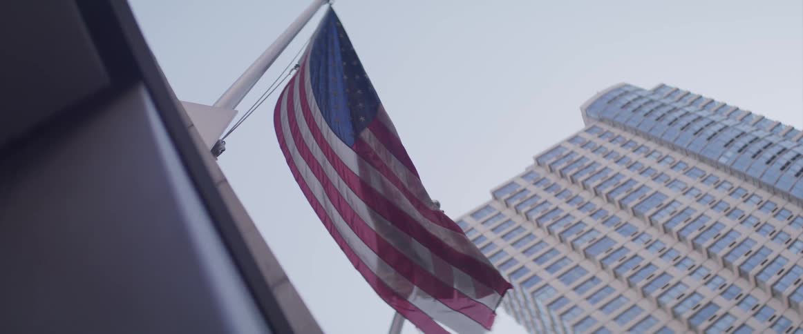 An american flag swaying in the wind while hanging from a flag pole on the facade of a building