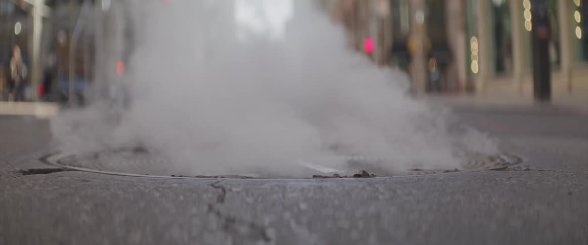 Steam rises from a manhole cover on a street in a city