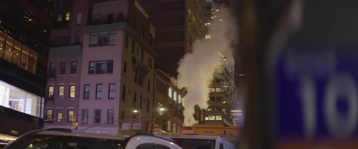 A city street with vehicles buildings and skyscrapers with steam coming out of a chimney