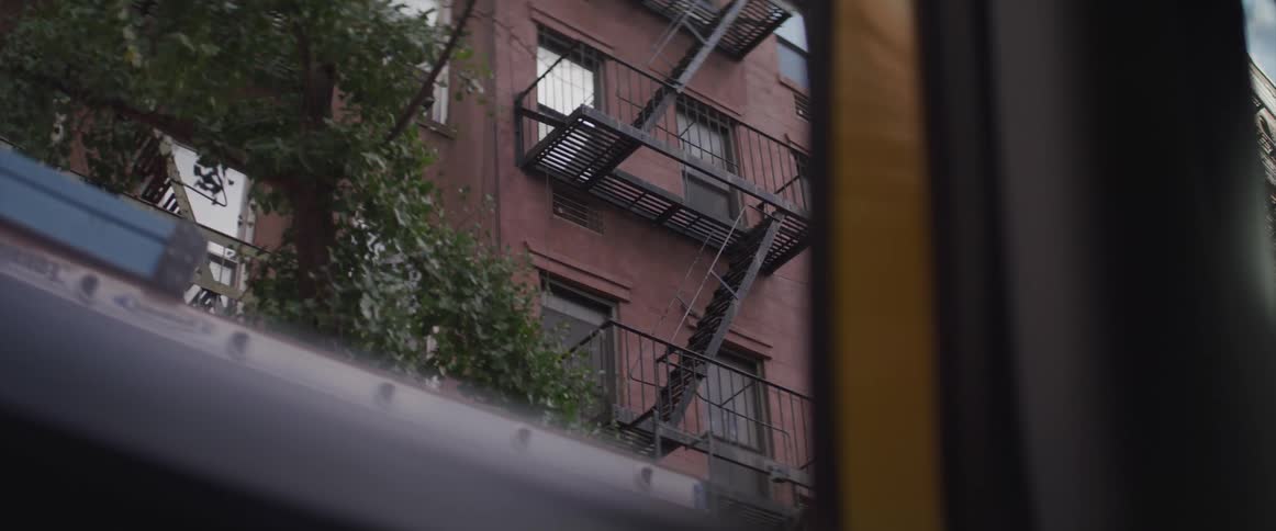 A box truck with a ladder drives past apartment buildings in a city