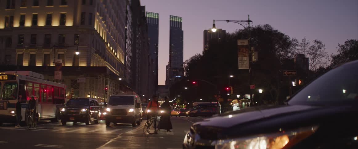 A vehicle turns a city corner as people cross an adjacent crosswalk