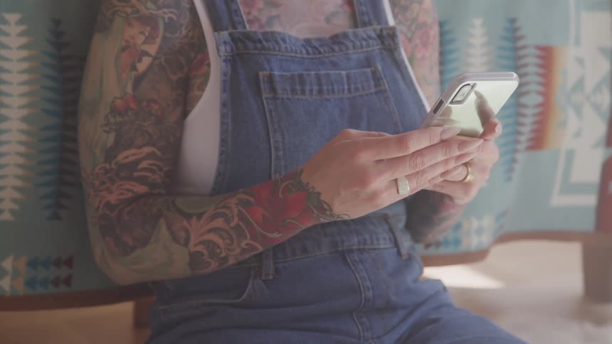 A woman with tattoos sitting down holding a smartphone