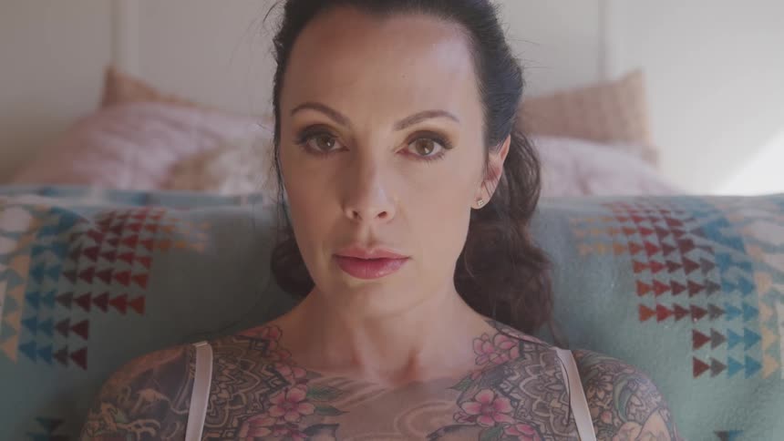 Tattooed woman sitting on the sofa turns her head and stares at the camera