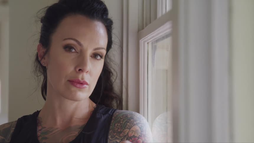 A white woman inside a room standing near a window