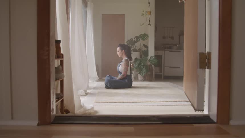 A woman sits on her floor and looks out the window