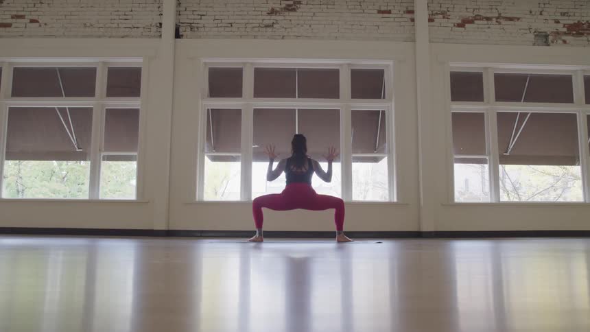 Woman moves through series of yoga poses on shiny wooden floor near windows