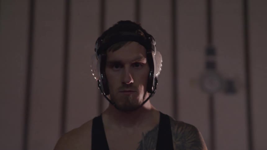 A man wearing a wrestling helmet and singlet standing in a dark