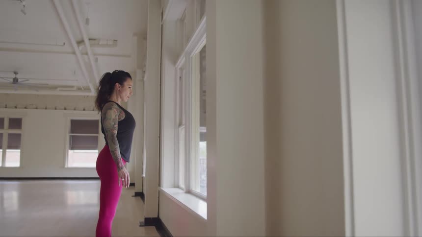 Woman inside dance studio stands in front of window looking outside