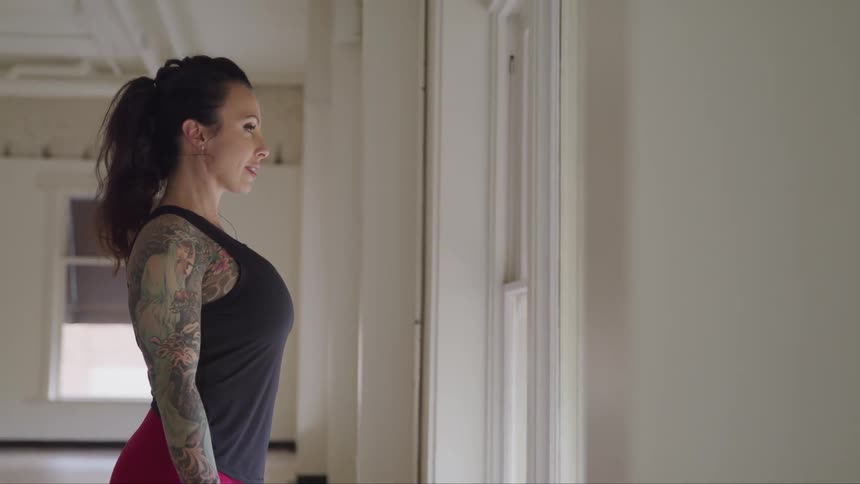Female with a tattoo sleeve wearing exercise apparel staring out the window while thinking and smiling slightly