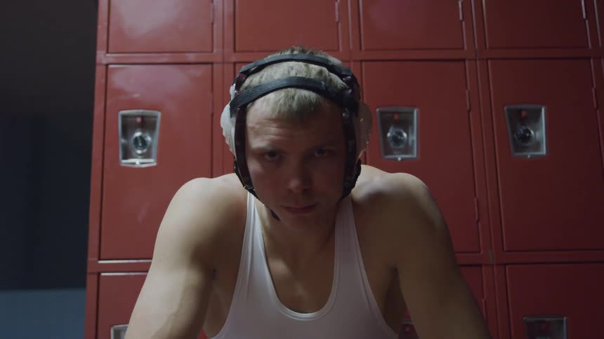 A wrestler sits by the lockers in a locker room