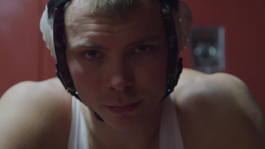 Young man in wrestling gear waits sitting in the locker room