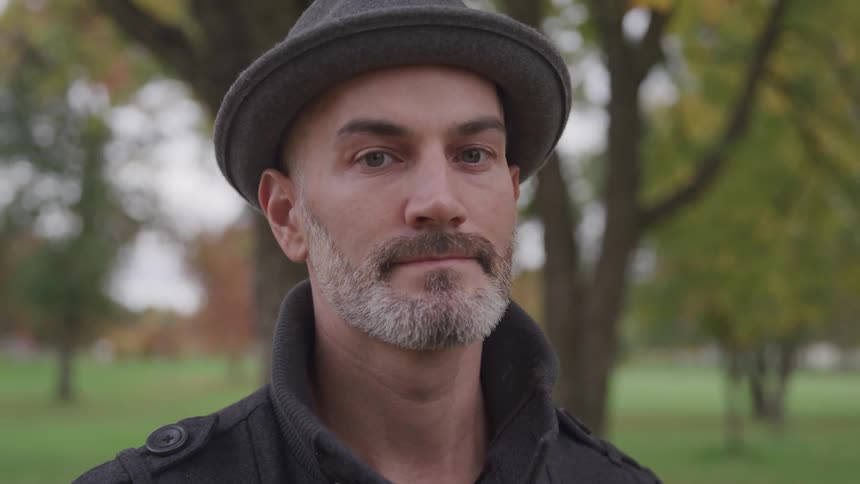 Man wears hat while standing outdoors near trees and wide lawn