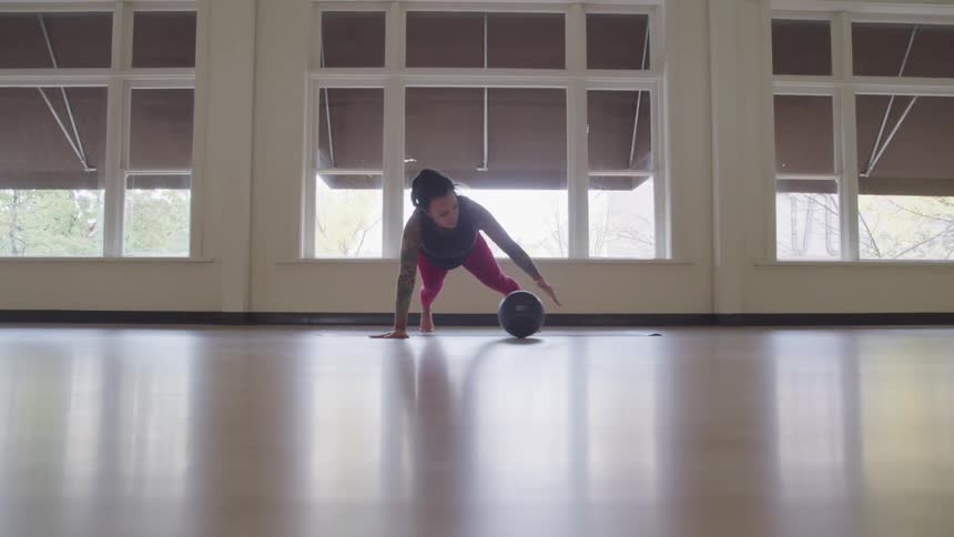 A woman exercises on the floor rolling a ball to her hands