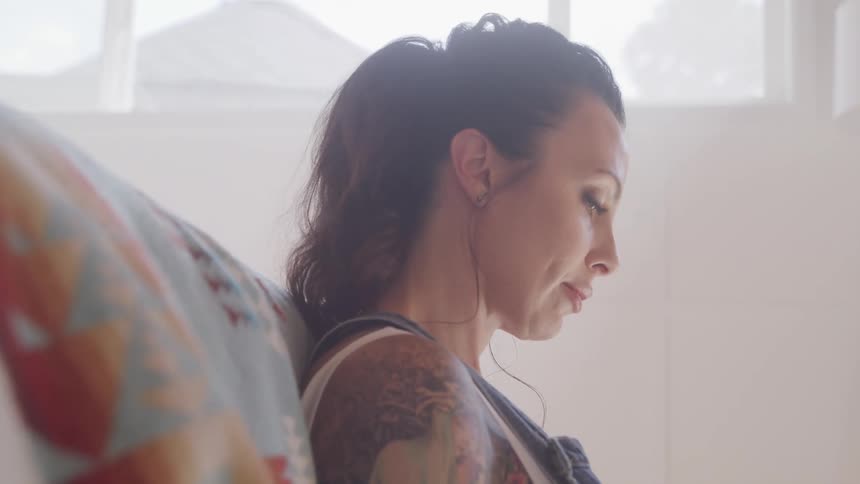 Tattooed woman sits on the sofa and looks down