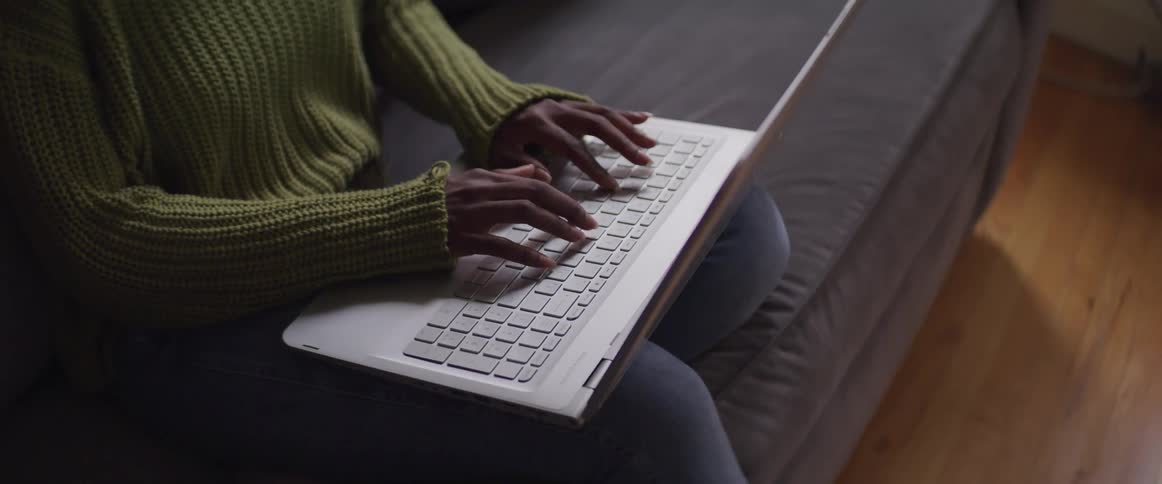 Woman sitting on the sofa types on the laptop in the living room at home