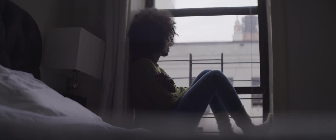 A young black woman sits and looks out the window