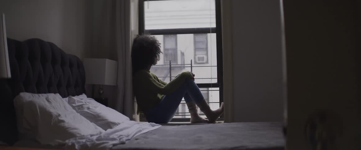 Woman sitting on window sill of bedroom and looking out