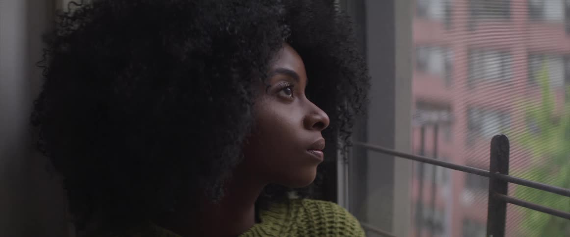 A woman sits next to and stares out the window of her apartment building