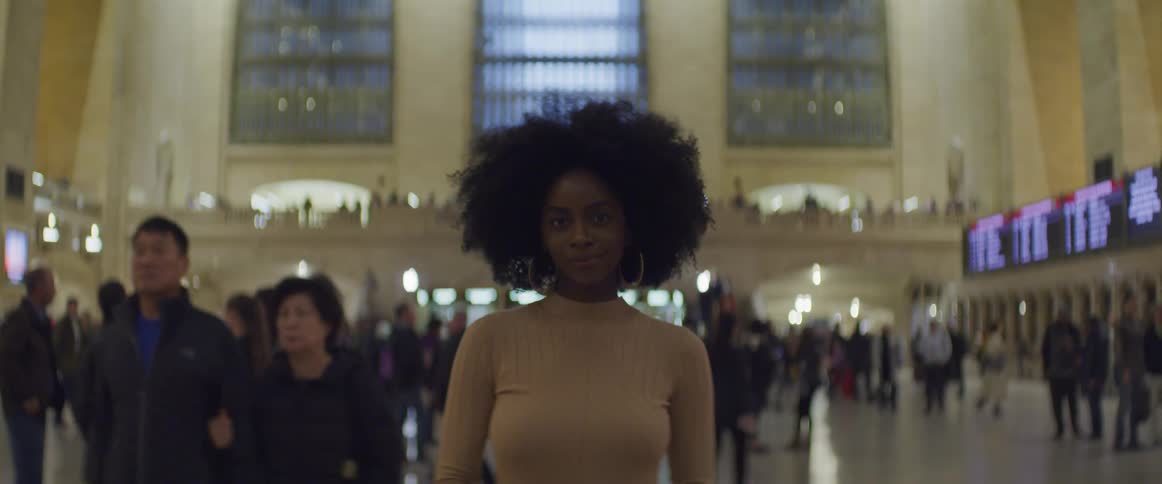 A woman poses standing in the middle of a busy train station
