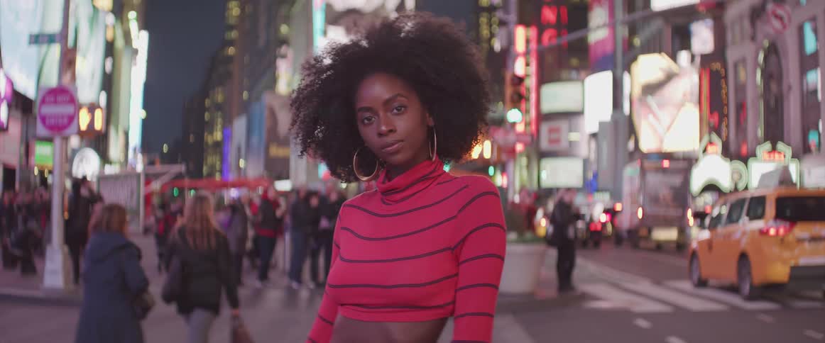 A woman stands in the center of a large city posing like a model