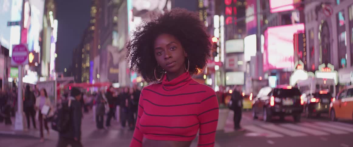 Black woman stands and poses for the camera in the busy street