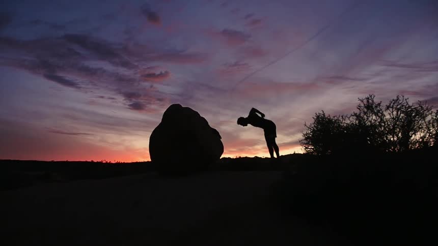 A man does a backflip from a boulder at sunset