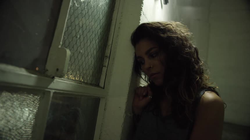 A white woman leans against the wall of a room by a window
