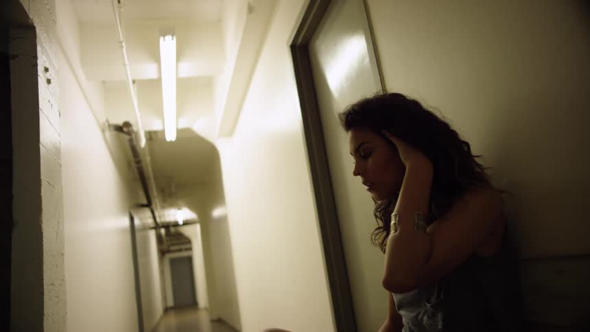 A teenager sitting in a hallway runs her fingers through her hair