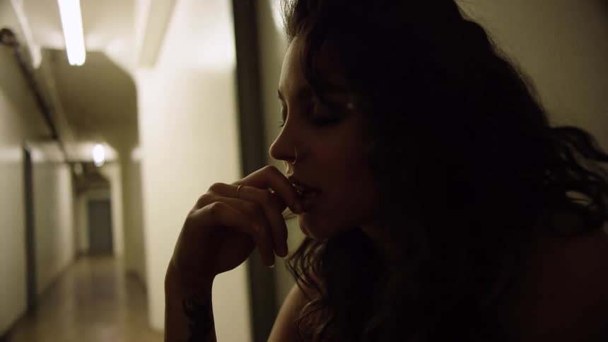 A woman smiles as she sits with her hand to her chin in an apartment hallway