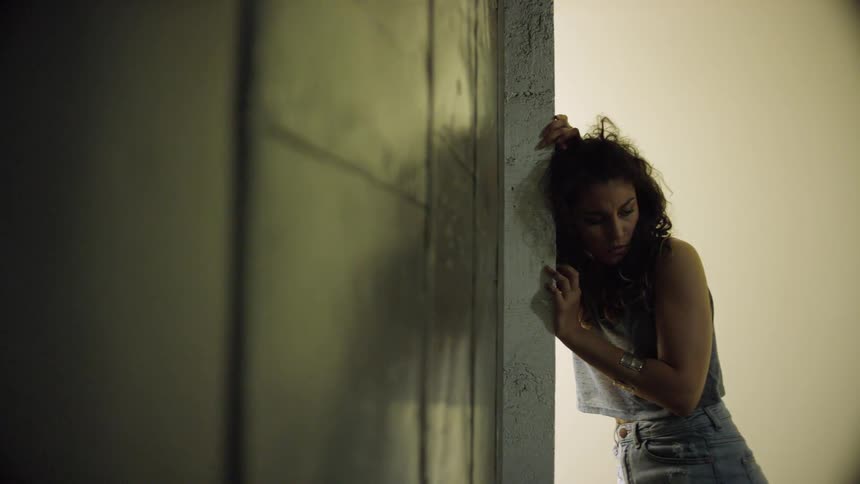 A woman stands with her head and hands against a cement wall
