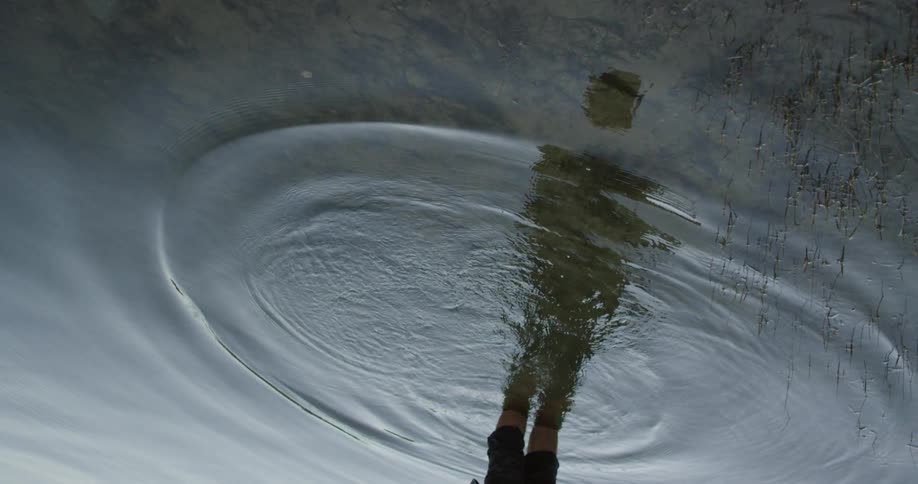 A mans silhouette is reflected in water after throwing a pebble in it