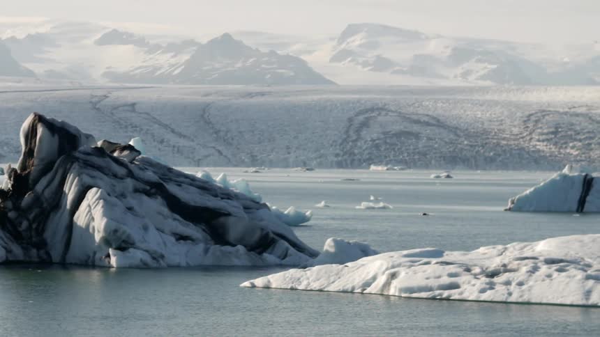 A row of icebergs sit in the water before a mountain range