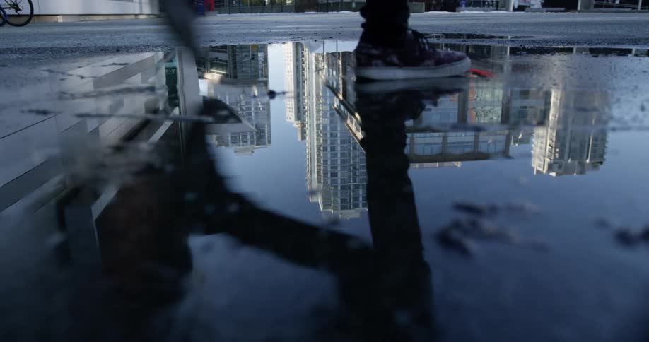 Person walks through street puddle reflecting skyscrapers