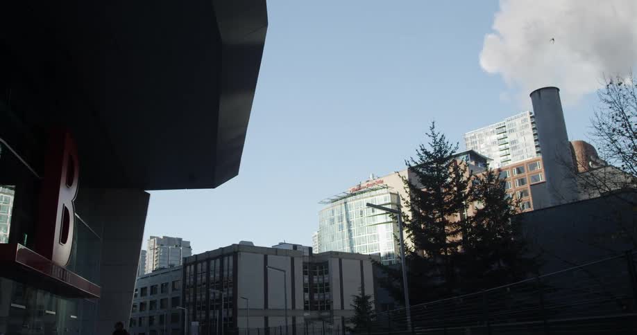 Smoke rises from a smokestack in front of tall office buildings in a city