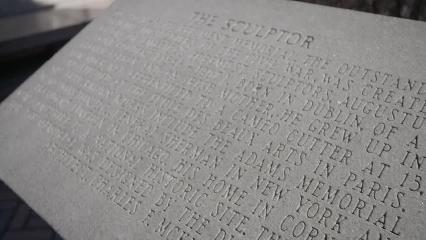 Carved stone plaque sits on marble base near tree