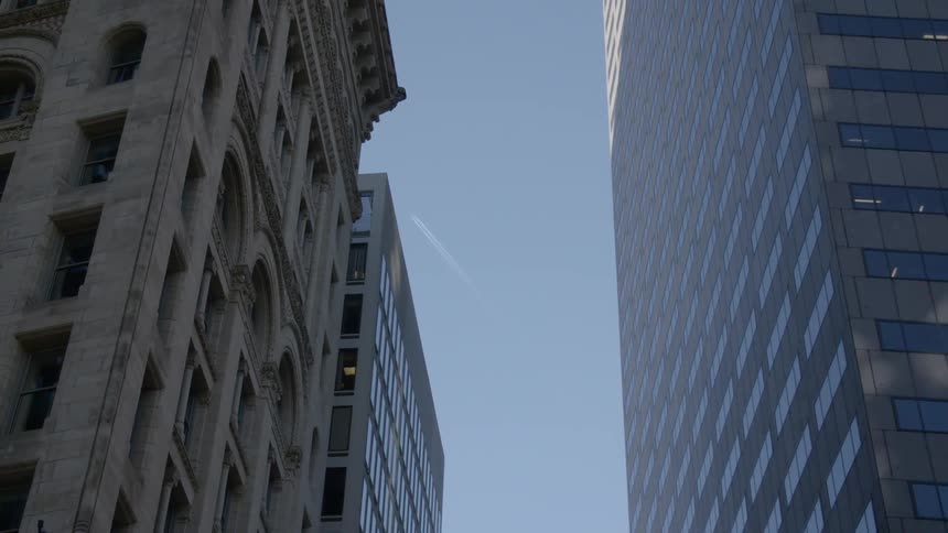 A city with buildings with the sky above with a contrail from a plane