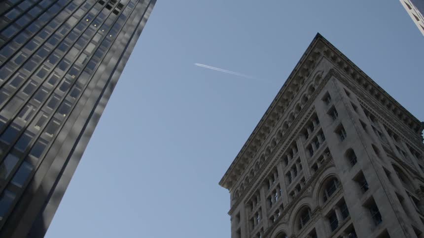 An airplane flies above office buildings and leaves smoke tracks