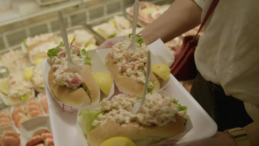 A woman holds a tray with three large lobster rolls