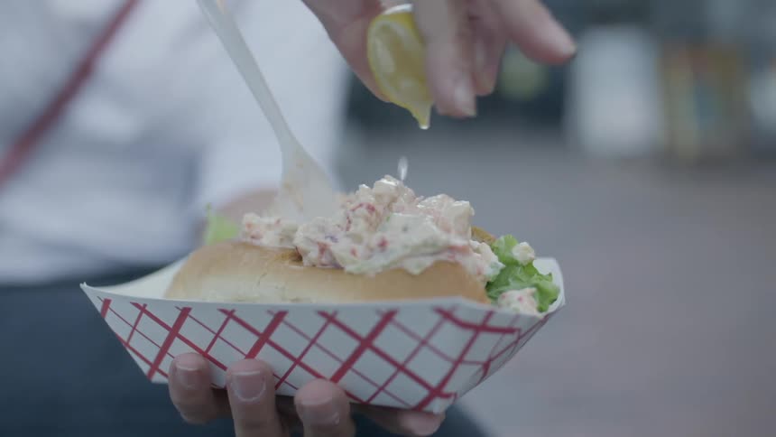 Close of a person squeezing lemon on chicken salad sandwich in food tray