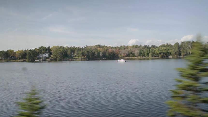 Footage of passing by a lake with a house and boat on it