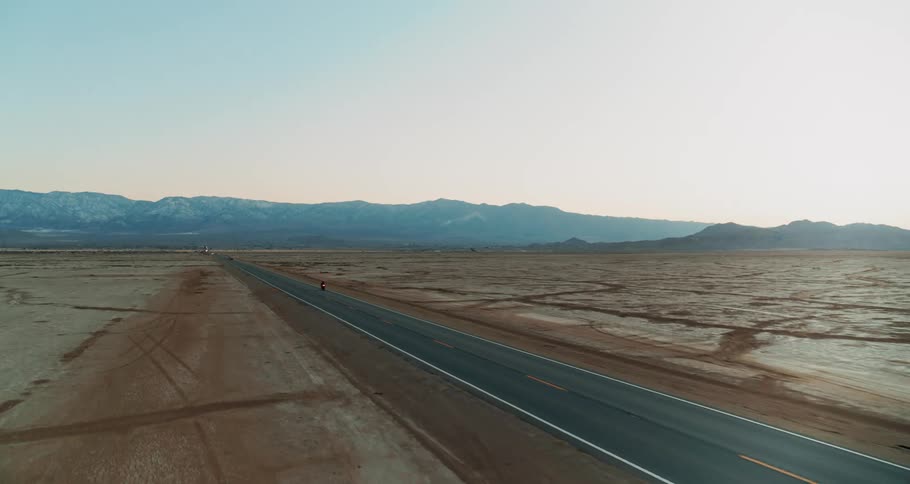 Motorcycle driving on a road through the desert at sunset