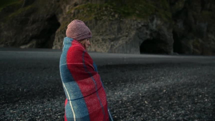 A woman is wrapped in a blanket as she stands by some caverns